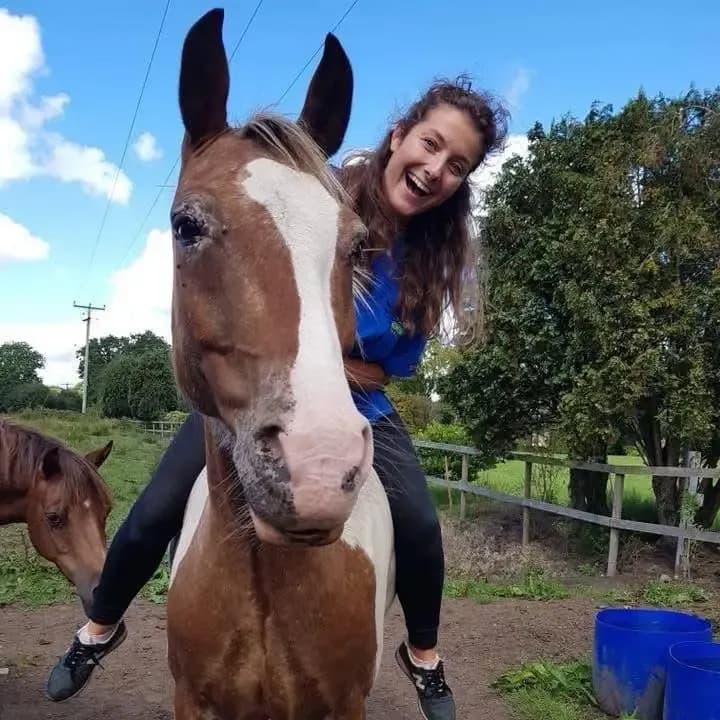 Dr Jenny Kurtz-Shefford laughing as she sits on a brown and white horse in a paddock