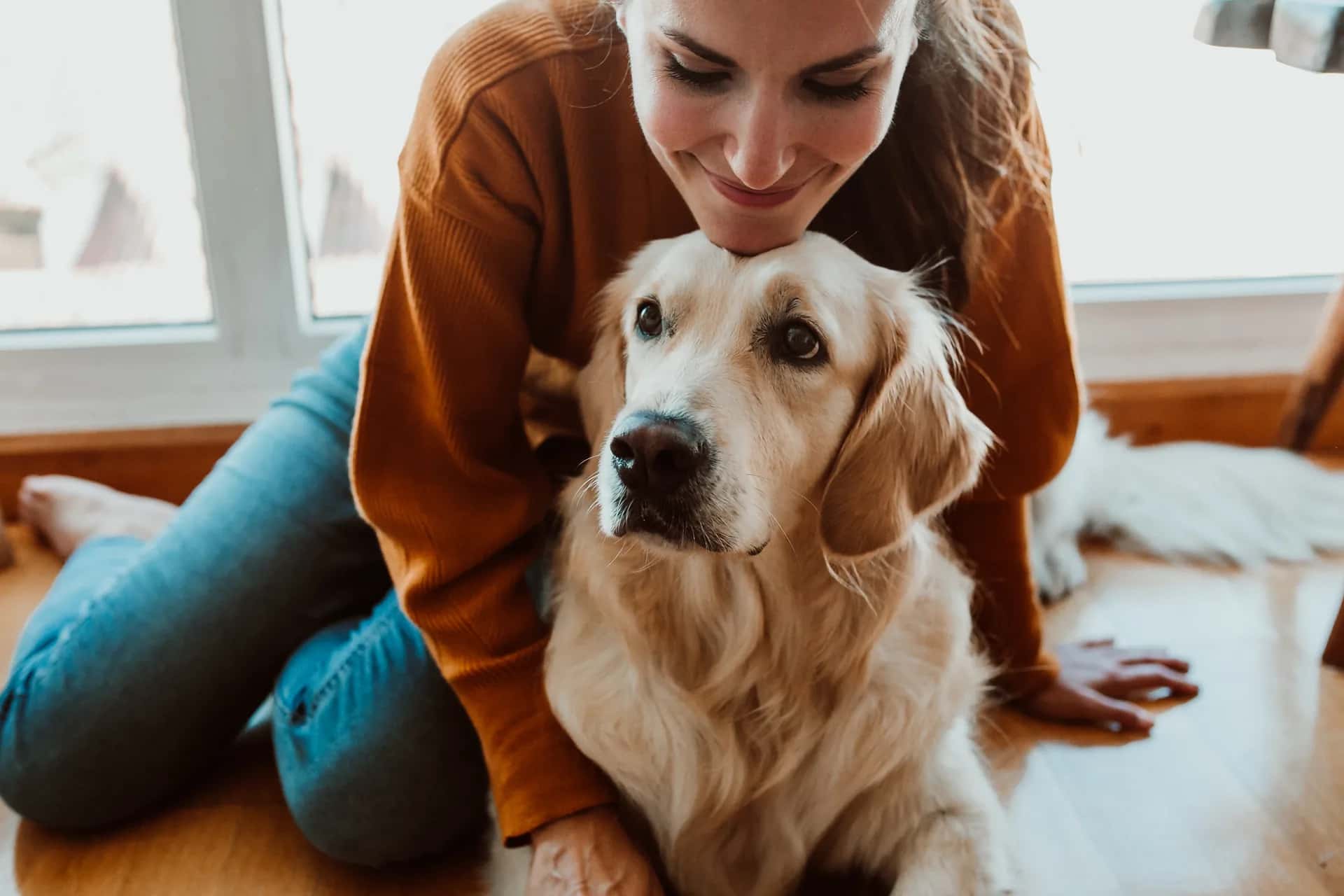 Woman kneeling on the floor at home, hugging her Golden Retriever